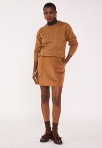 Pull en tricot marron avec un col rond, associé à une jupe en laine avec des poches avant, et des chaussures marron avec des accents décoratifs.