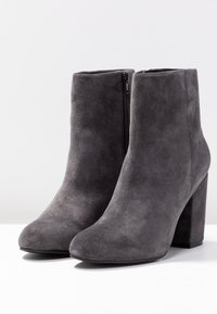 Bottines en suède gris avec une pointe arrondie, un talon bloc haut et une fermeture éclair sur le côté. Texture lisse et design simple.
