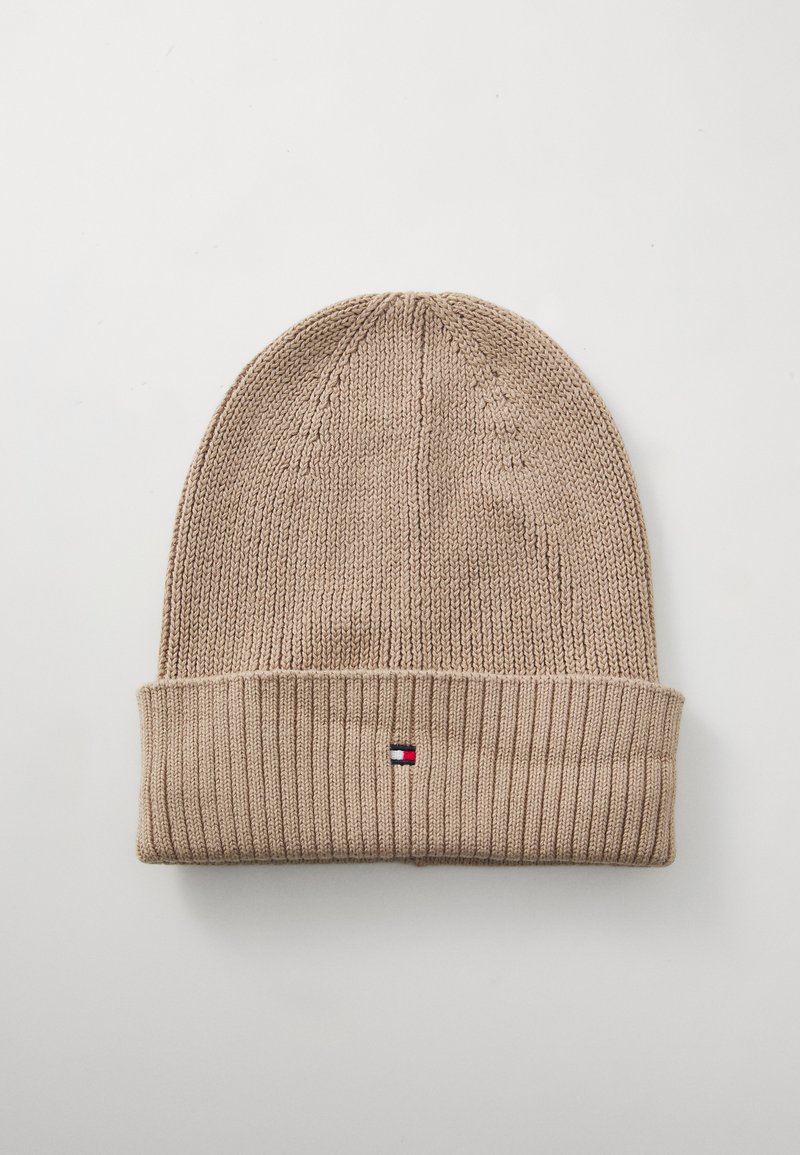 Beige strikket lue med ribbestrikket kant. Har et lite logomerke med røde, hvite og blå detaljer. Myk tekstur, middels tykkelse.