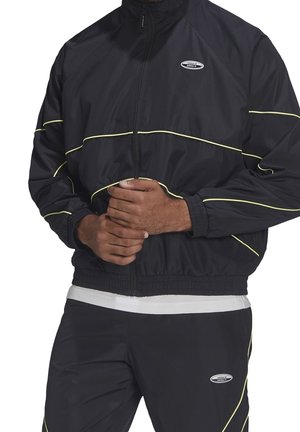 Zwart sportjack met gele accentstrepen, ritssluiting, opstaande kraag en elastische manchetten. Voorzien van het merklogo op de linkerbovenborst.