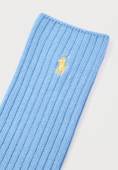 Ανοιχτό μπλε ύφασμα με ραβδώσεις και μια μικρή κίτρινη κεντημένη φιγούρα παίκτη του πόλο σε απλό λευκό φόντο.