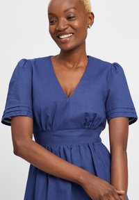 Blue dress with a deep V-neck, short puff sleeves, and a fitted bodice. Smooth texture with pleated detailing at the waist. Casual design.