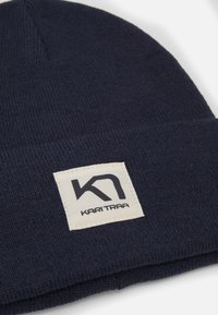 Laine beanie marine tricoté avec un revers replié et une étiquette carrée tissée avec du texte noir. La texture est lisse avec un léger côtes.