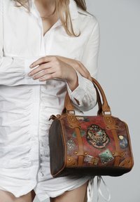 Sac à main en cuir marron avec texture embossée, patches rouges et verts, accents décoratifs et poignées en cuir. Présente des détails en matériel doré.