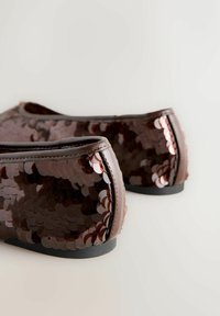 Pantofi plate maro, acoperiți cu paiete strălucitoare, având vârful rotunjit și o talpă joasă neagră. Textura este netedă, cu un ușor luciu.