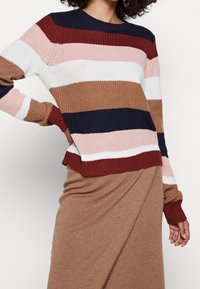 Stickad tröja med flerfärgade horisontella ränder i vinröd, marinblå, rosa, brun och vit; ribbade ärmslut och nederkant; har en rund halsringning.