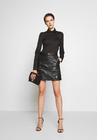 Black long-sleeve shirt paired with a black leather mini skirt featuring silver hardware accents and zippered pockets, held with a black handbag.