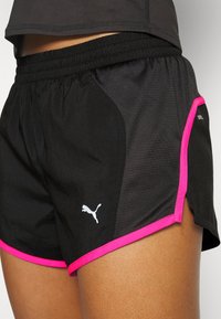 Svarta atletiska shorts med en ventilerande meshdesign, med rosa sidodetaljer och en vit Puma-logga på nedre vänstra sidan.