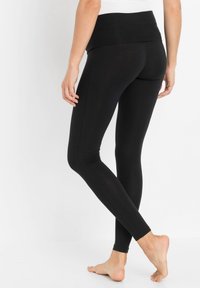 Leggings noirs en tissu extensible avec une large taille. Texture lisse, design ajusté et look sans couture le long des jambes.