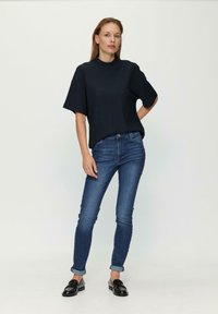 Ciemnoniebieska, prążkowana bluzka z krótkim rękawem połączona z dopasowanymi dżinsami z niebieskiego denimu z podwiniętymi mankietami oraz czarnymi loafersami. Prosta, nowoczesna sylwetka.