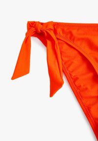 Jasnopomarańczowe majtki bikini z węzłem po boku, gładką strukturą i cienkimi ramiączkami podkreślającymi wysoki krój.