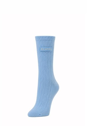 Chaussette côtelée bleu clair avec un revers plié et une étiquette rectangulaire cousue indiquant "OH APRIL" sur le côté.