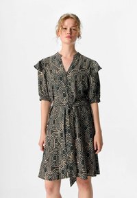 Svart och krämfärgad mönstrad klänning med V-ringning, korta puffärmar och knytning i midjan. Tyget har cirkulära mönster och texturerade detaljer.