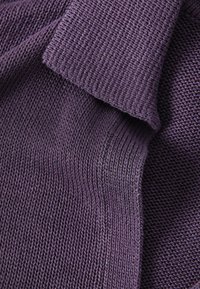 Gros plan sur un tissu tricoté violet plié montrant des motifs de points détaillés et la texture.