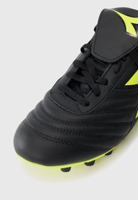 Black football boot with textured leather upper, laces, and neon green accent. Features stitched details and traction studs on the sole.