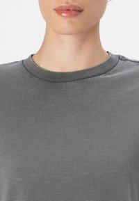 Grijze t-shirt met een ronde hals, gladde textuur en korte mouwen. De stof lijkt zacht en licht gemêleerd.