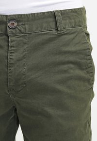 Olivegröna bomullbyxor med dragkedja och knäppning, bälteshällor och framfickor med en slät yta.