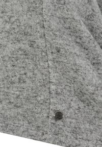 Tessuto di maglia grigio con una trama sottile e un motivo maculato, dotato di un piccolo adesivo metallico attaccato alla cucitura inferiore.