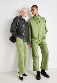 Črn-bel črtast srajčen gumb s dekorativno opremo, v kombinaciji z zelenim vzorčastim kompletom in kontrastnimi črnimi čevlji.