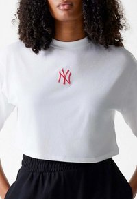 Witte cropped t-shirt gemaakt van zacht materiaal, met een rood geborduurd logo in het midden, een ronde halslijn en relaxed gesneden mouwen.