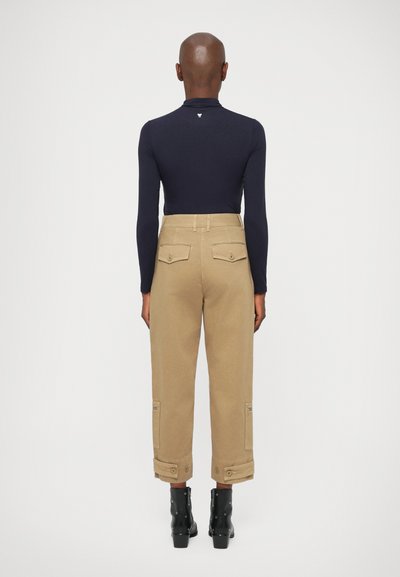 Bluză albastră cu mâneci lungi, pantaloni cargo khaki cu buzunare pe spate, manșete răsucite și bocanci negri cu accesorii din argint. Design minimalist.