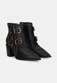 Botas de cuero negro hasta el tobillo con puntas afiladas, acentos de tachuelas doradas y dos correas con hebillas. Los tacones en bloque aportan estabilidad y soporte.