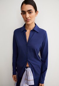 Donkerblauwe lange mouwen shirt met knoopsluiting en kraag, met een gladde textuur en een subtiel vallende pasvorm. Gestyled met een lichtblauwe strikaccent.