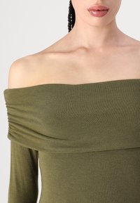 Olivenfarget off-the-shoulder topp med ribbet tekstur, med draperinger langs utringningen og lange ermer.