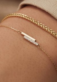 Bracelet en or avec deux accents rectangulaires : un en or lisse et un en argent texturé. Porté sur la peau avec un bracelet en or tressé au-dessus.