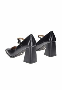 Scarpe nere in pelle con tacco a blocco, punta appuntita, cinturino alla caviglia e fibbia rotonda. Texture liscia con una finitura lucida.