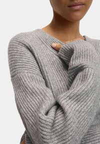 Grauer Strickpullover mit gerippter Textur, tiefem V-Ausschnitt und übergroßen Ärmeln, der weiches Garn und eine lässige Passform zeigt.