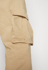 Pantalones cargo beige, con un bolsillo lateral, material de algodón suave, corte recto y costuras visibles a lo largo de las costuras.