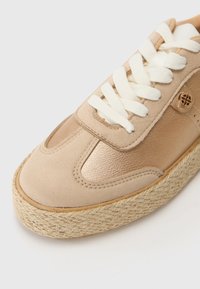 Beige uformelt sneakers med overdel i lær og semsket skinn, bomullsneller og såle dekket med jute. Har sømdetaljer og metallsymbol.