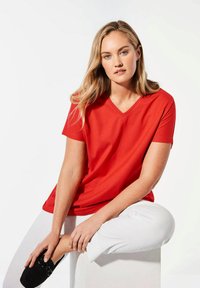 Rode korte mouwen V-hals t-shirt van zachte stof, met een ontspannen pasvorm. Gepaard met witte broek en zwarte schoenen. Minimalistisch ontwerp.
