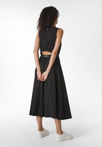 Abito nero senza maniche con dettaglio sulla schiena a taglio, gonna fluida e vita elastica; abbinato a sneaker bianche. Tessuto morbido, design minimale.