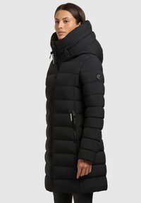 Must must coat kõrge kraega, lukuga taskud ja vertikaalne õmblus. Omab kitsast siluetti ja siledat, tekstuurset kangast.