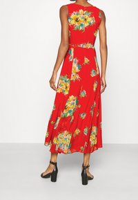 Röd blommig maxiklänning med en utsvängd kjol, prydd med livliga gula och gröna blommönster. Slät tyg, ärmlös design och rund nacke.