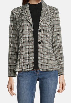 Blazer à carreaux gris, noir et blanc avec deux boutons à l'avant, revers crantés et épaules structurées. Associé à un haut noir et un jean bleu.