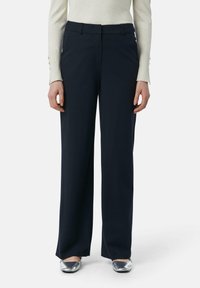 Marineblauwe wijde broek met een gladde textuur, een platte voorkant en riemlussen, gecombineerd met metallic zilveren schoenen en een lichtgekleurde top.