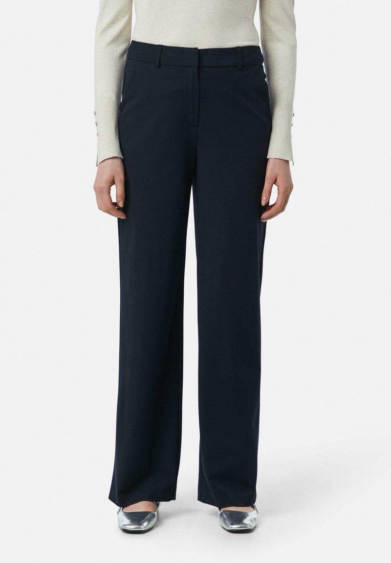 Marineblauwe wijde broek met een gladde textuur, een platte voorkant en riemlussen, gecombineerd met metallic zilveren schoenen en een lichtgekleurde top.