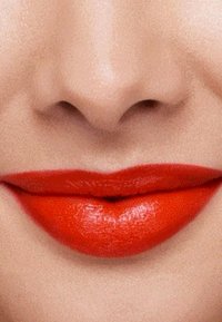 Błyszcząca czerwona pomadka na pełnych ustach, charakteryzująca się gładką teksturą i wyraźnym kształtem, na tle neutralnego odcienia skóry.