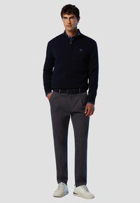 Marinefarbener Zip-Pullover, graue Hose und weiße Sneakers. Der Pullover hat ein Logo auf der Brust; die Hose hat eine maßgeschneiderte Passform und eine glatte Vorderseite.