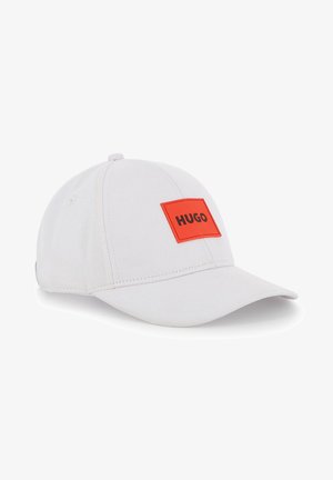 Casquette de baseball blanche en tissu avec un patch rectangulaire rouge vif affichant "HUGO" en lettres noires sur le devant.