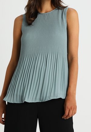 Top plisado sin mangas de color azul claro usado con pantalones negros, mostrando tejido texturizado y un ajuste relajado desde los hombros hasta la cintura.