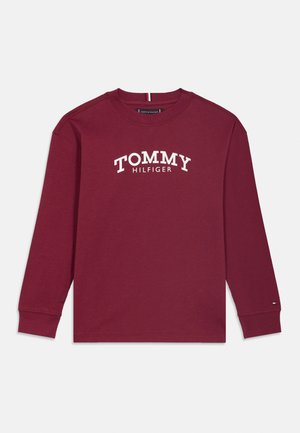 Burgunderfarbener Langarm-T-Shirt aus Baumwolle, mit einem weißen "TOMMY HILFIGER"-Logo, das quer über die Brust gedruckt ist, sowie einem kleinen Logo-Akzent am Ärmel.