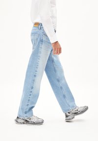 Lichtblauwe denim jeans met een relaxte pasvorm, met een gemiddelde taillehoogte en subtiele vervaging. Gecombineerd met grijze sneakers en een wit shirt.
