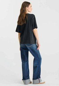 Camiseta de algodón negra de gran tamaño combinada con unos jeans de mezclilla azules con puños. La camiseta tiene mangas cortas y un corte relajado, sin patrones.