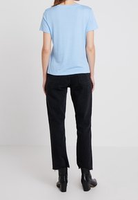 Svetle modré bavlněné tričko s kulatým výstřihem, spárované s černými rovnými džíny s nerovným lemem, nošeno s kotníkovými botami.