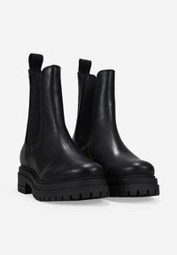 Botas Chelsea de cuero negro con paneles laterales elásticos, suela de plataforma gruesa y un acabado suave. Diseño minimalista sin herrajes visibles.