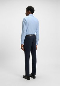 Vaaleansininen pitkähihaisessa paidassa on kuvio, joka on yhdistetty tummansinisiin housuihin. Musta vyö ja kengät täydentävät asukokonaisuutta.